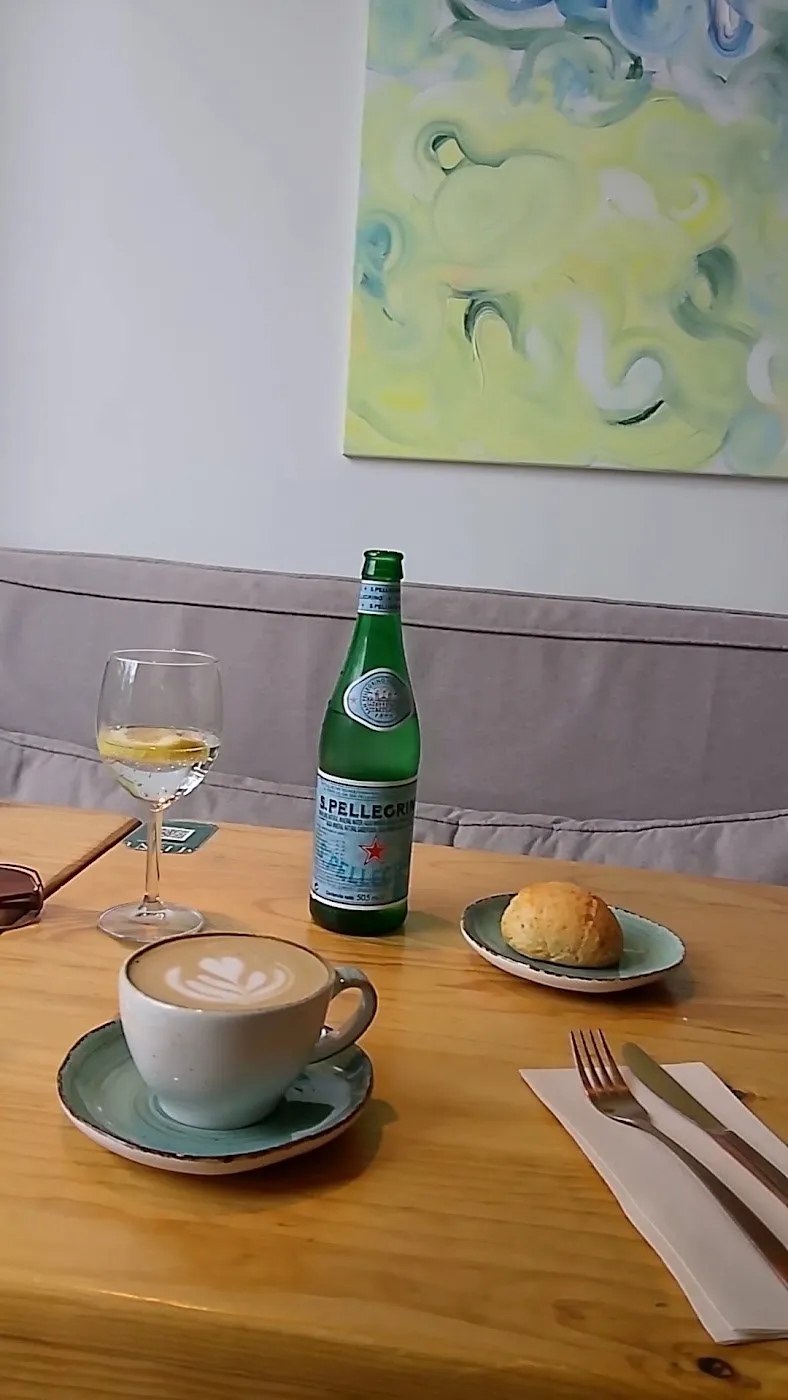 Mesa con un café, un panecillo y una botella de agua junto a un cuadro de tonos verdes