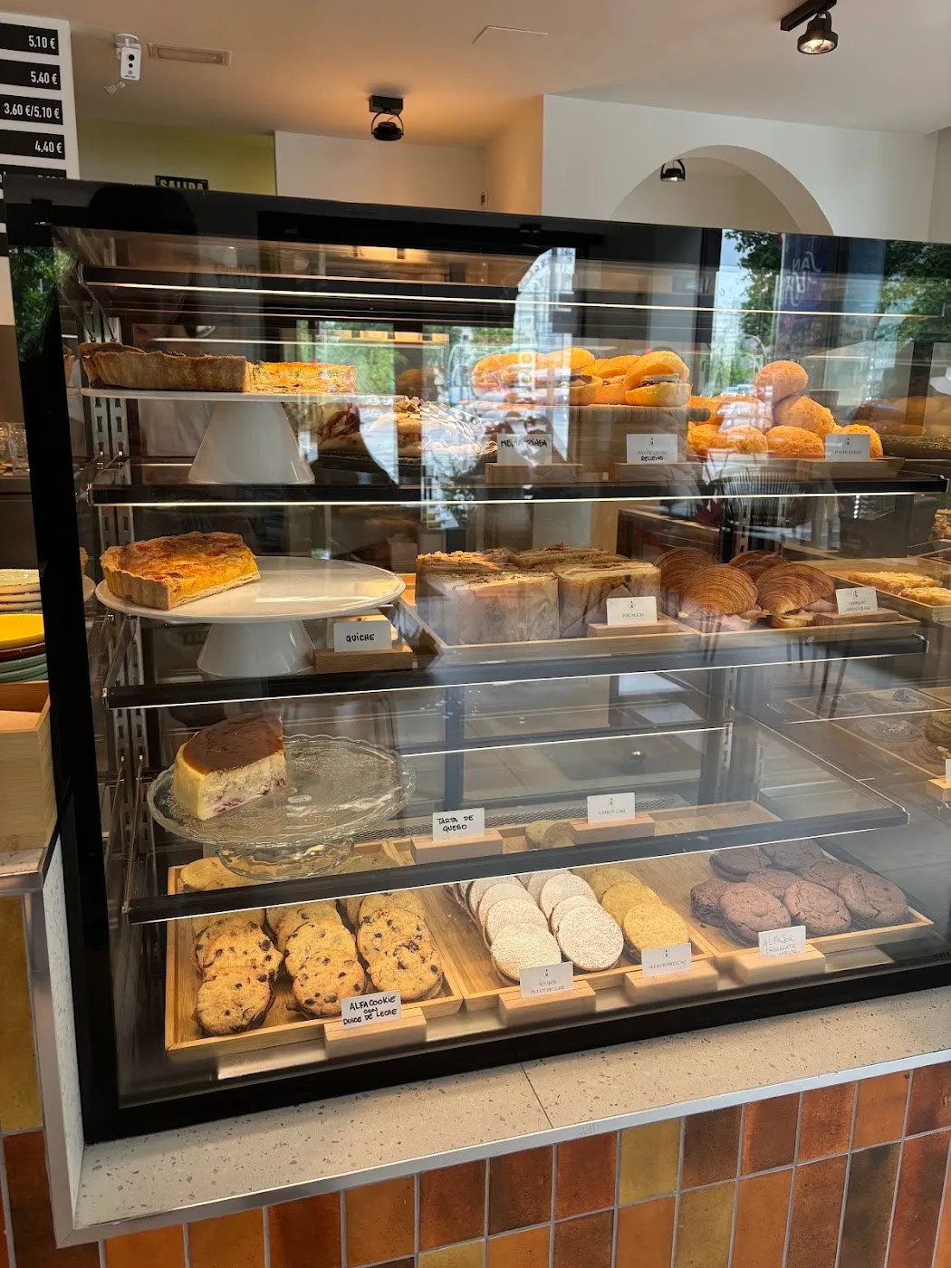Vitrina de cristal con tartas, bollería y galletas sobre un mostrador de azulejo