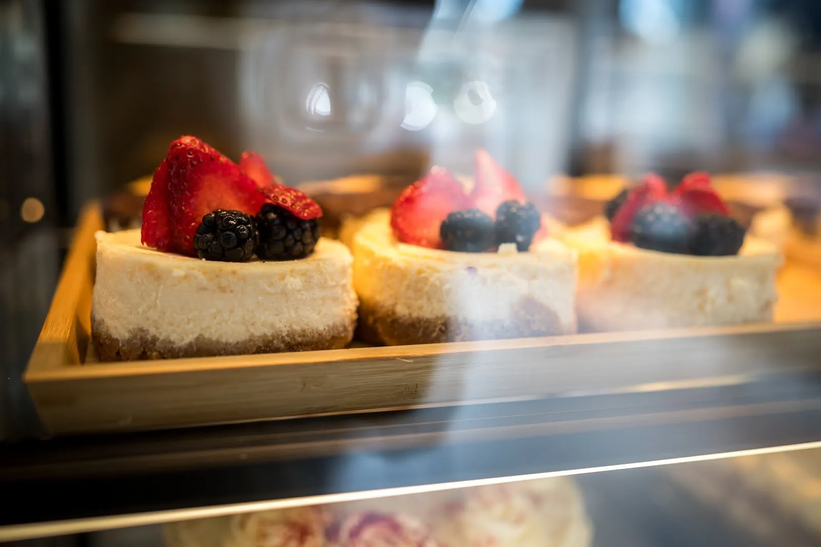 Tres cheesecakes con fresas y moras sobre una bandeja de madera en la vitrina