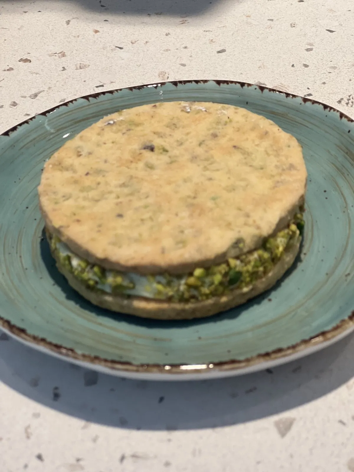 Alfajor de pistacho relleno de crema y rebozado en pistacho en un plato turquesa