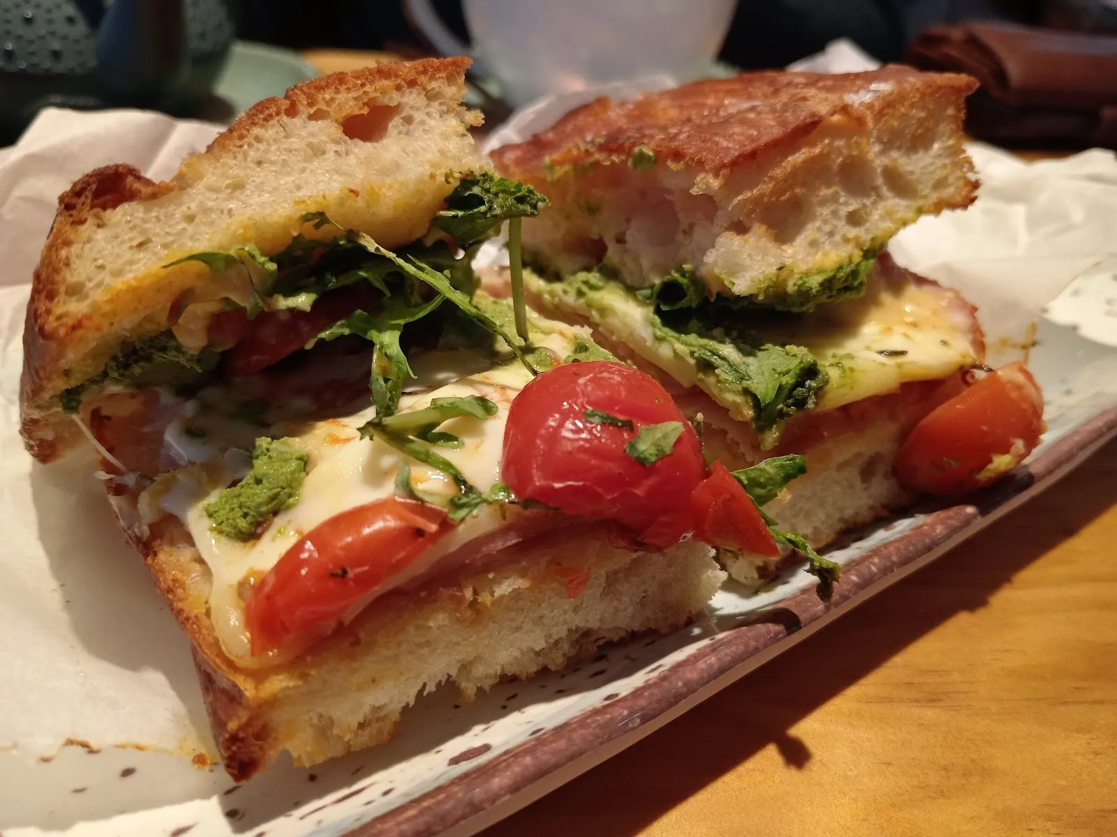 Focaccia partida rellena de queso fundido, embutido, tomates asados, pesto y rúcula